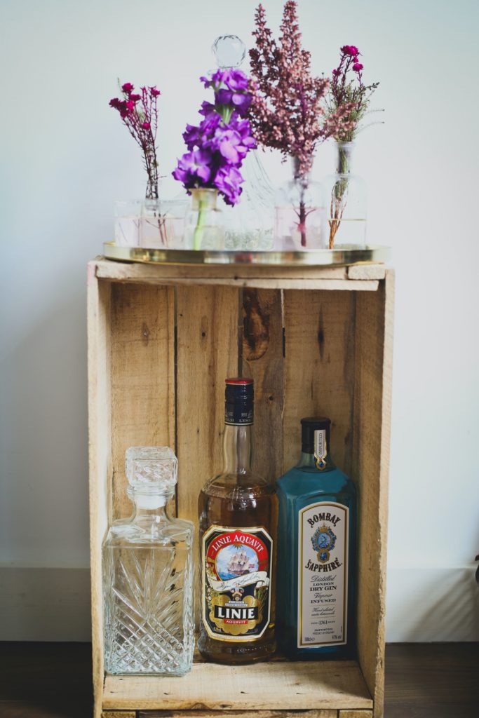 Tiny wooden shelf with three alcoholic drinks inside and a flower on top